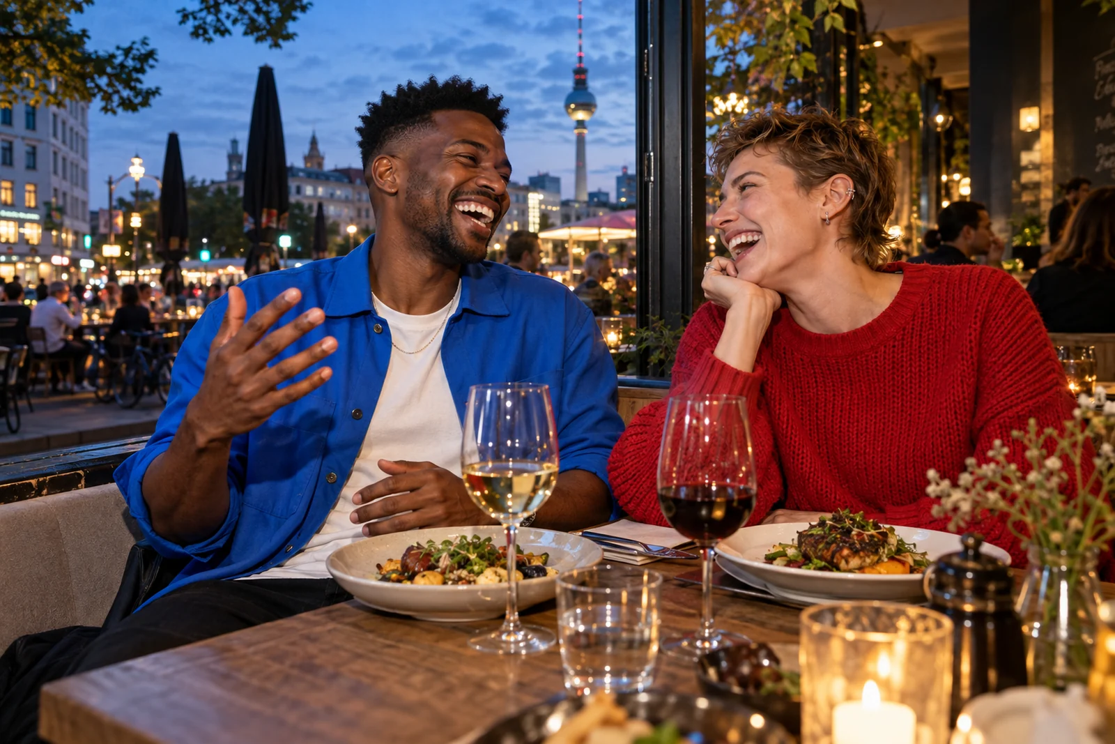 Zwei Freunde essen am Fenster eines Berliner Restaurants mit Blick auf den Fernsehturm bei Abendlicht