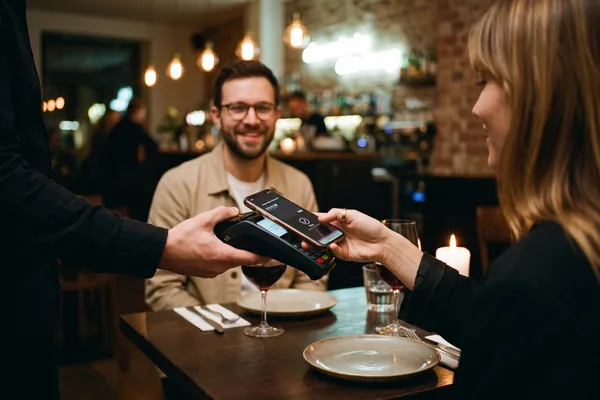A woman pays in a restaurant with the Atento gift card in her smartphone wallet